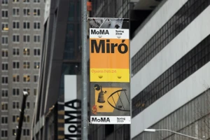 MoMA outdoor vertical banner advertising a Miro exhibition mounted on a city street pole with skyscrapers behind