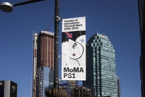 Vertical street banner for MoMa PS1 exhibition set against urban skyscrapers and a clear blue sky