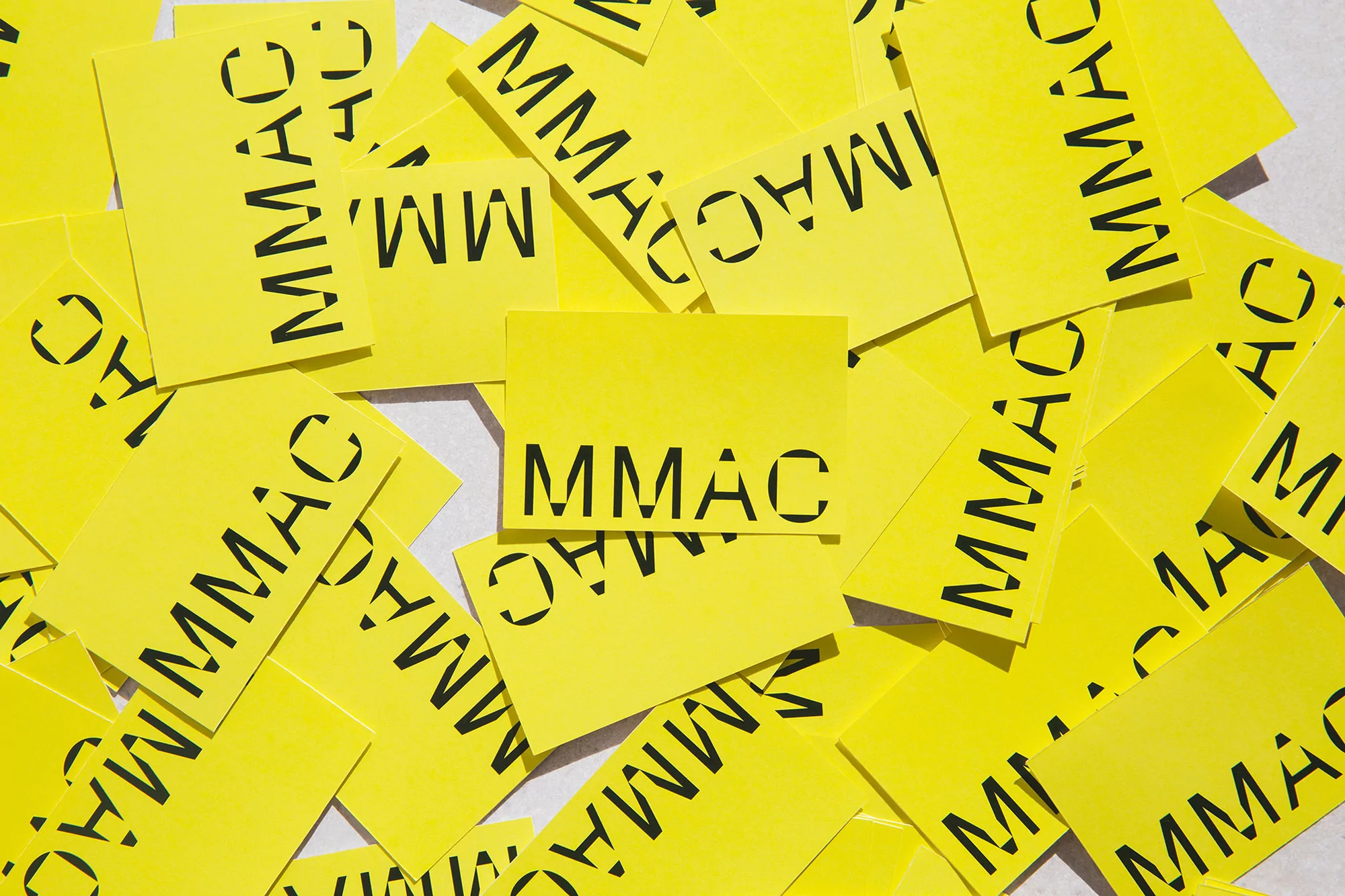 Overhead shot of scattered yellow cards with the text 'MMAC' in black, creating a pattern of organized chaos.