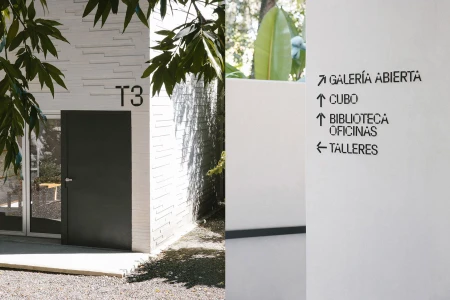Exterior architectural signage for MMAC featuring bold typography on white walls and a dark door labeled T3.