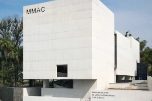 Modern white concrete building exterior featuring the MMAC logo and clear geometric architectural lines under a blue sky