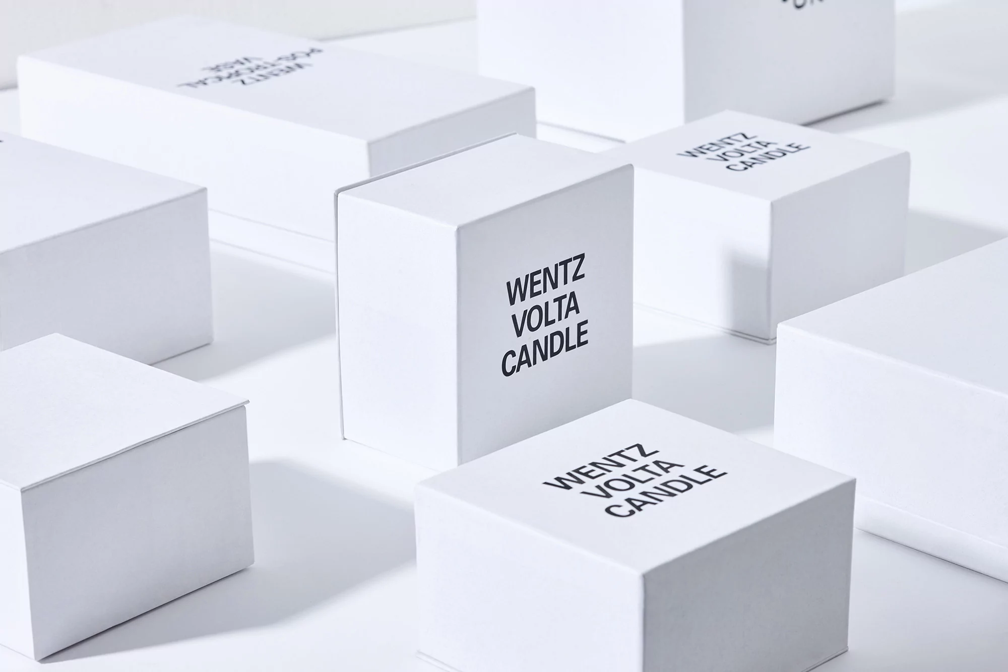Multiple white, cube-shaped product boxes with black text labels are arranged on a white surface with a soft, diffused lighting effect.