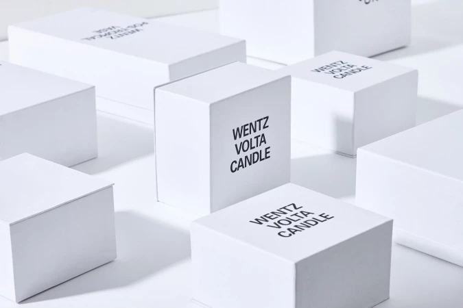 Multiple white, cube-shaped product boxes with black text labels are arranged on a white surface with a soft, diffused lighting effect.