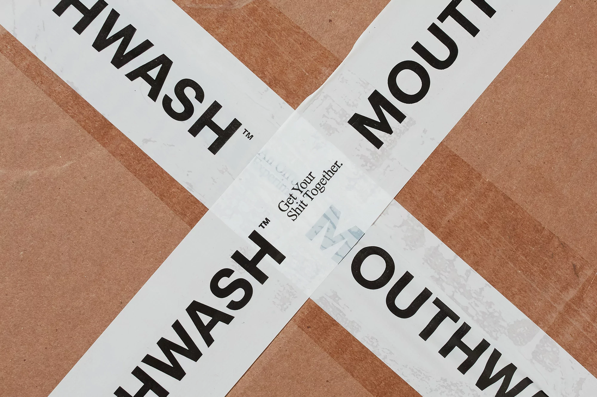 Top-down, close-up studio shot of a sealed brown cardboard box with white tape forming an X. The tape is printed with 'Mouthwash'.