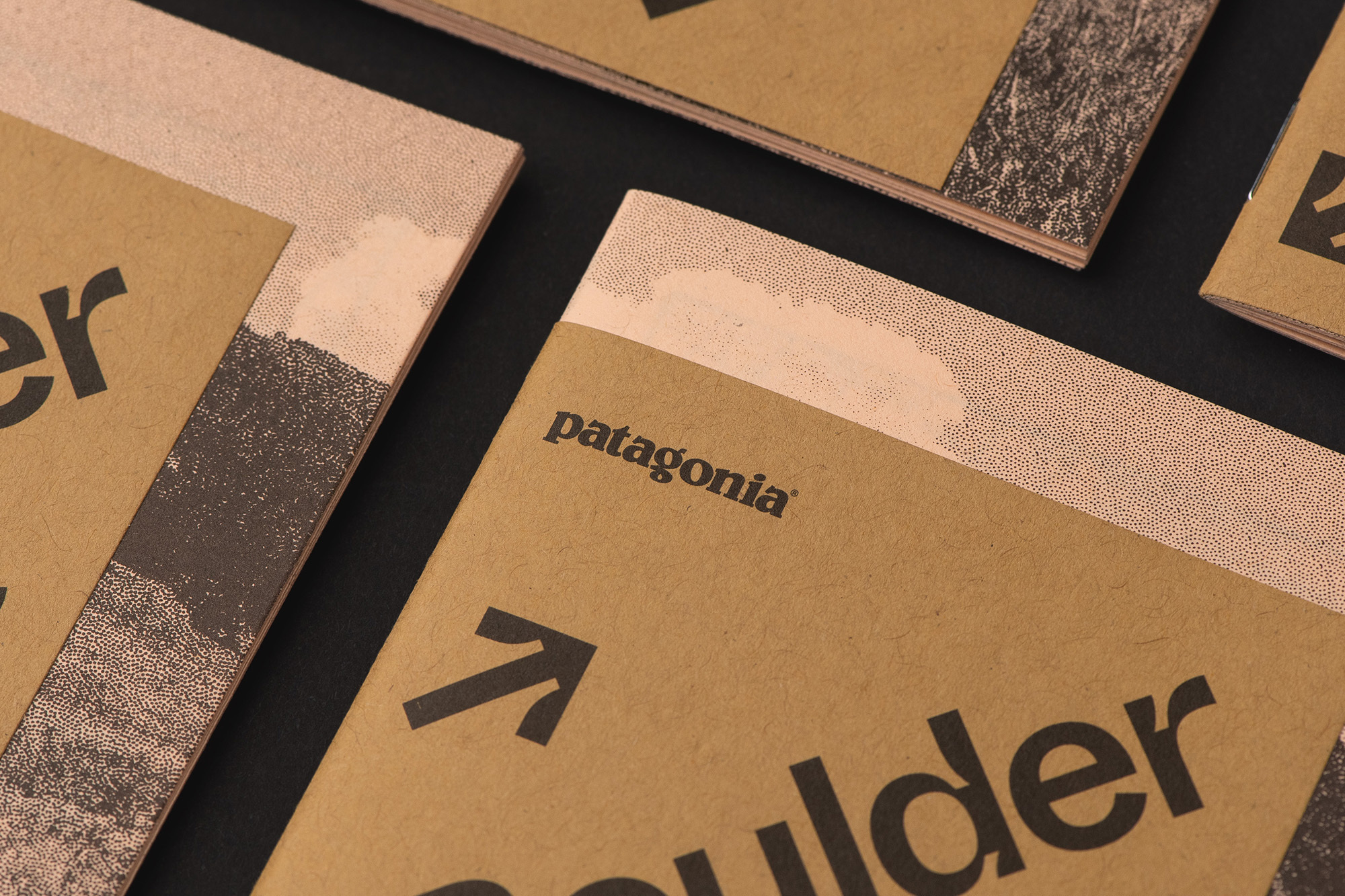 Close-up of multiple tan-colored Patagonia booklets with black text and graphics, displayed on a dark background. 
