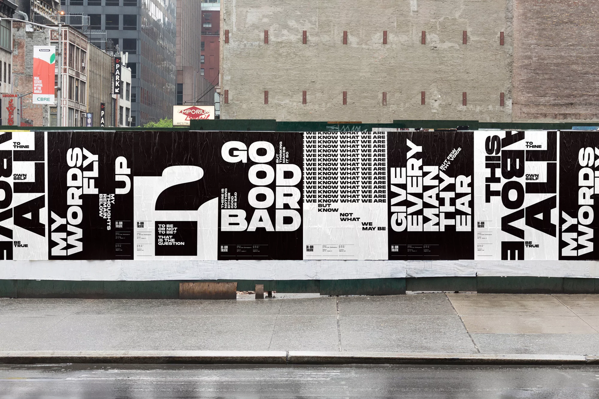 Eye-level shot of black and white posters with bold typography mounted on a green wall, set against an urban background.