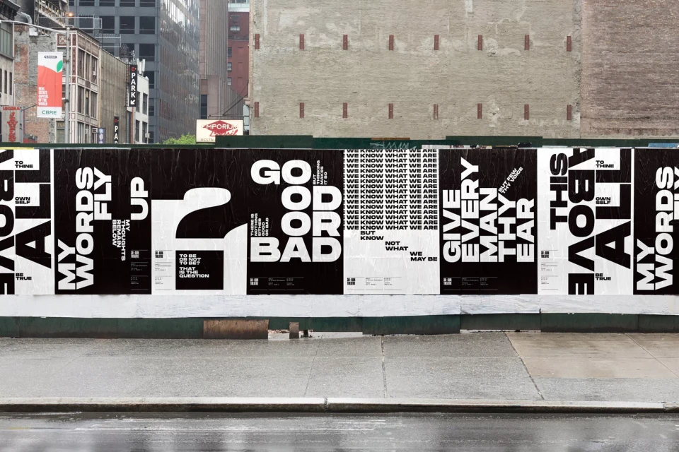Eye-level shot of black and white posters with bold typography mounted on a green wall, set against an urban background.