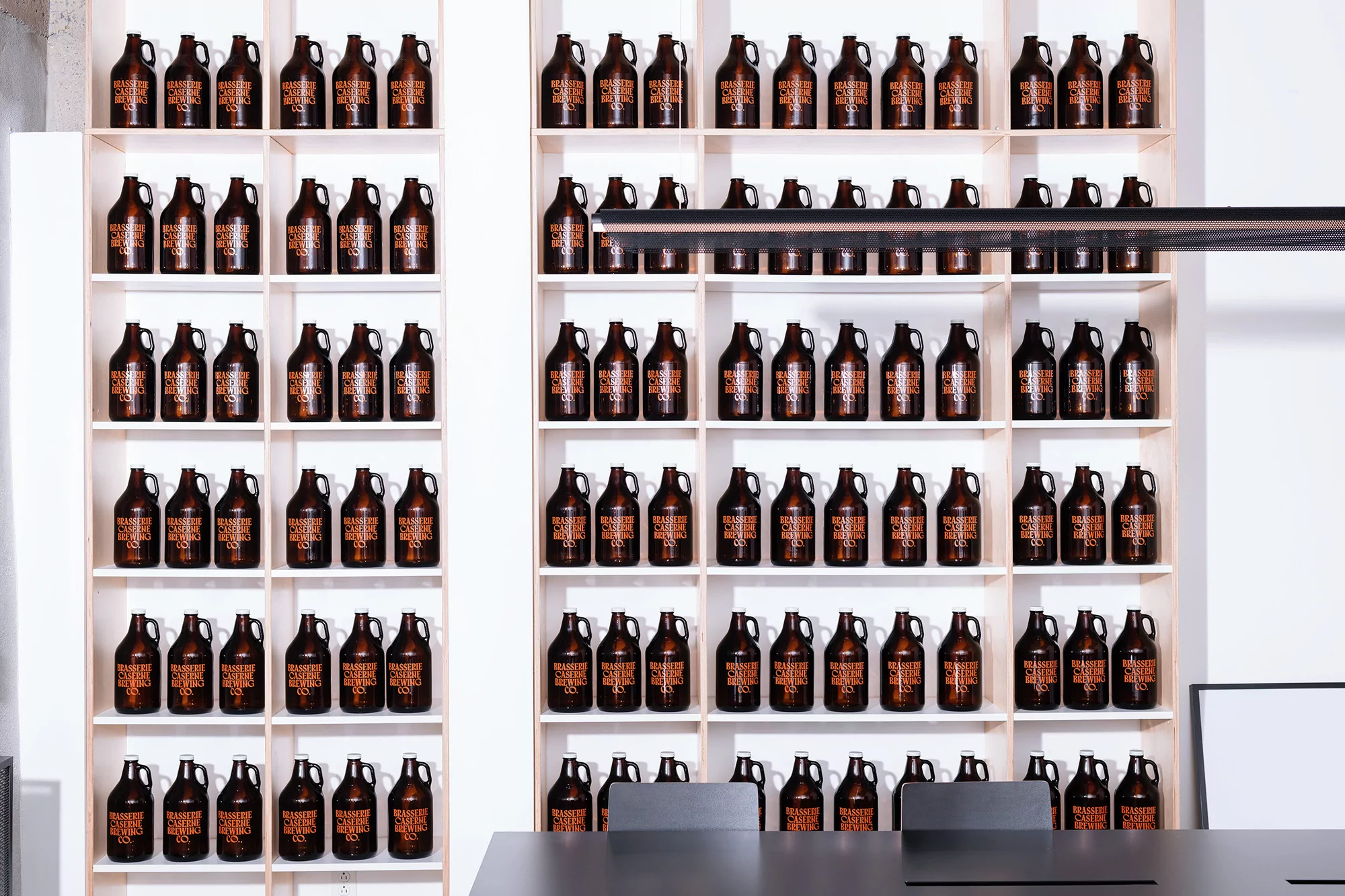 Shelves filled with rows of brown glass growlers, creating a symmetrical and visually appealing display in a modern setting.