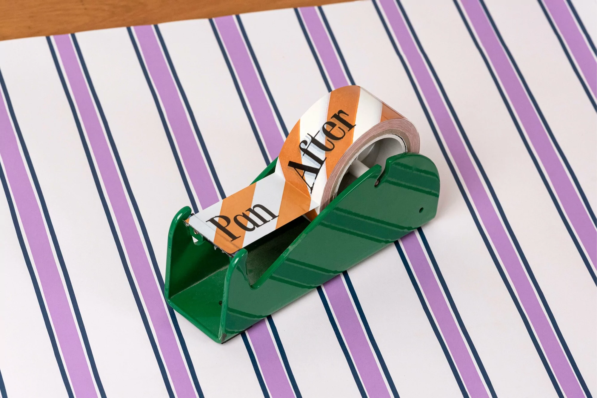 Close-up of a green tape dispenser with striped tape on a striped surface, showcasing office supplies and geometric patterns.