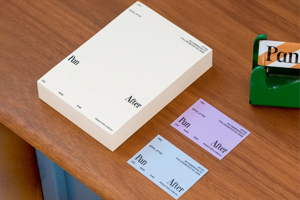 Eye-level shot of a cream stationery set with business cards, featuring 'Pan After' branding, set on a wooden desk. Minimalist design.