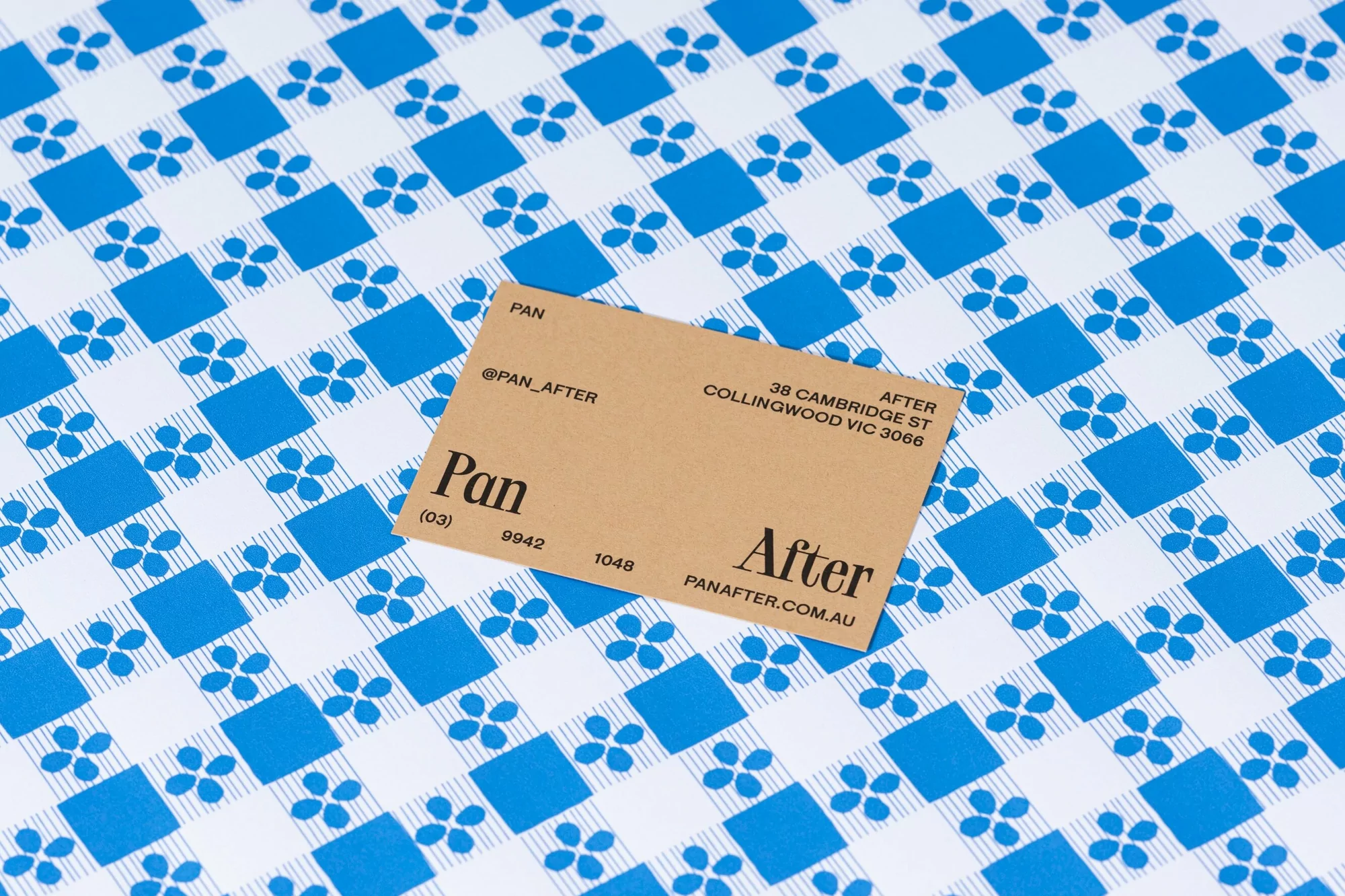 Promotional product shot of a tan business card on a blue and white patterned background with floral and square accents.
