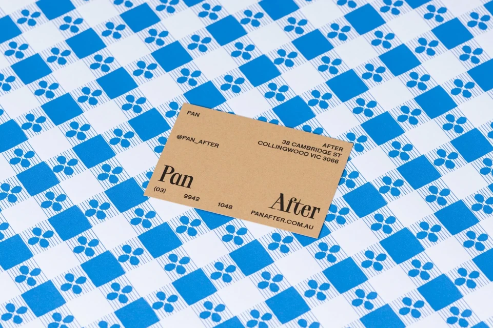 Promotional product shot of a tan business card on a blue and white patterned background with floral and square accents.