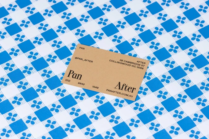 Promotional product shot of a tan business card on a blue and white patterned background with floral and square accents.