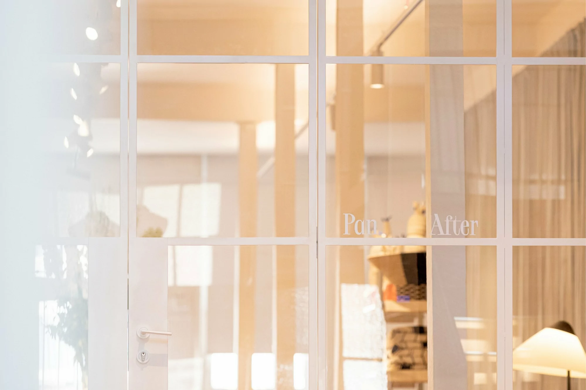 Bright, naturally lit room seen through a white-framed glass door with text; modern interior design with warm tones and a glimpse of furniture.