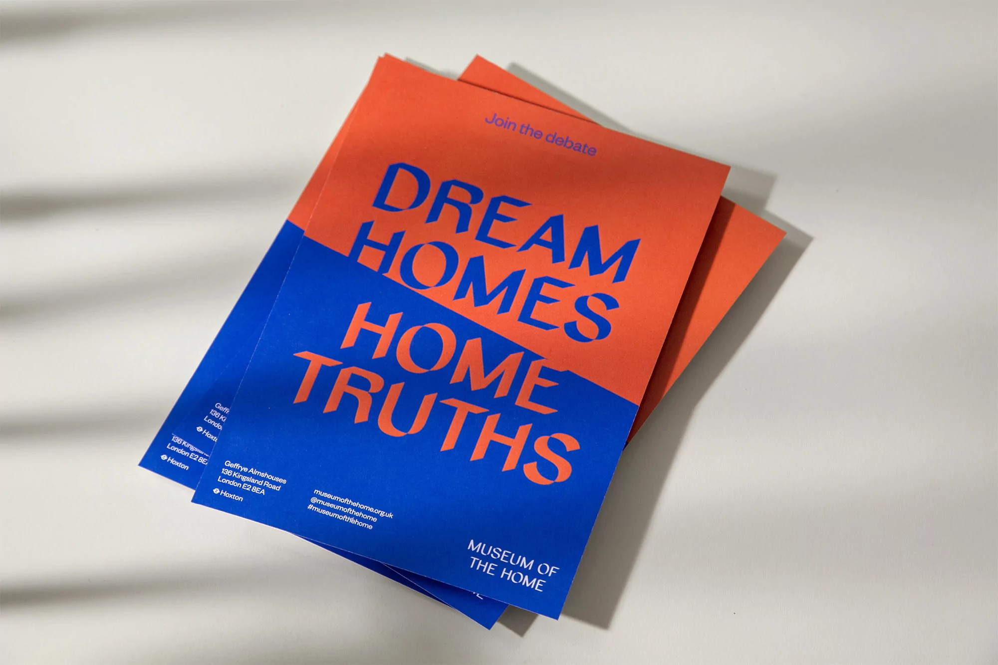Stack of Museum of the Home brochures featuring the phrase 'Dream Homes Home Truths' in blue and orange on a white surface with shadows.