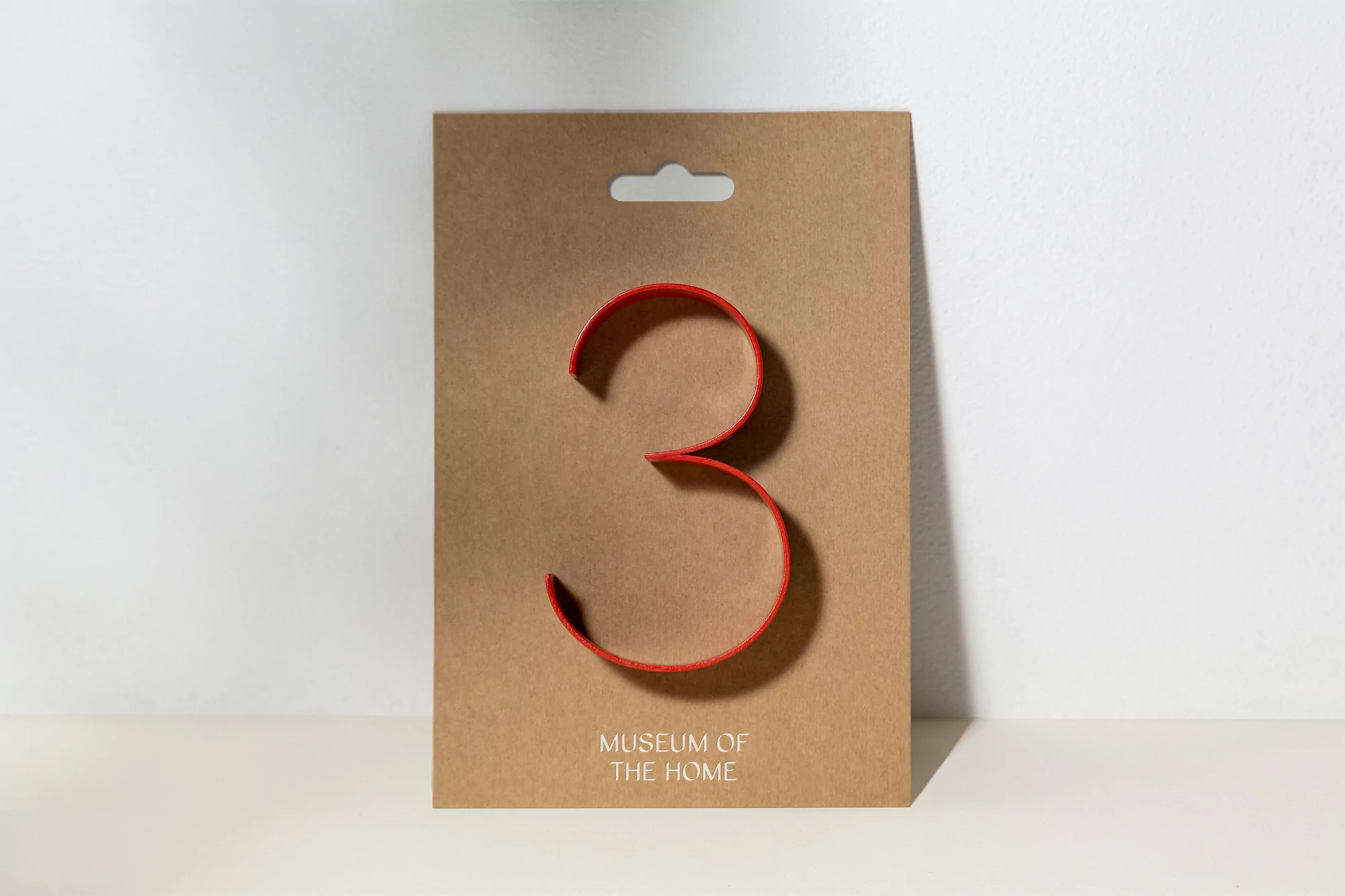 Stylized red number three on a tan display card against a white background. The card has 'Museum of the Home' printed on the lower portion.