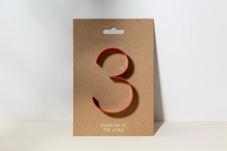 Stylized red number three on a tan display card against a white background. The card has 'Museum of the Home' printed on the lower portion.