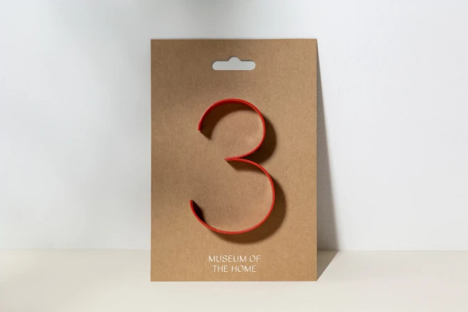 Stylized red number three on a tan display card against a white background. The card has 'Museum of the Home' printed on the lower portion.