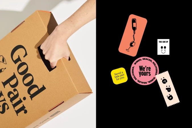 Hand grips handle of a branded cardboard delivery box; sticker graphics feature stylized bottle, wineglass, and cheerful typography.