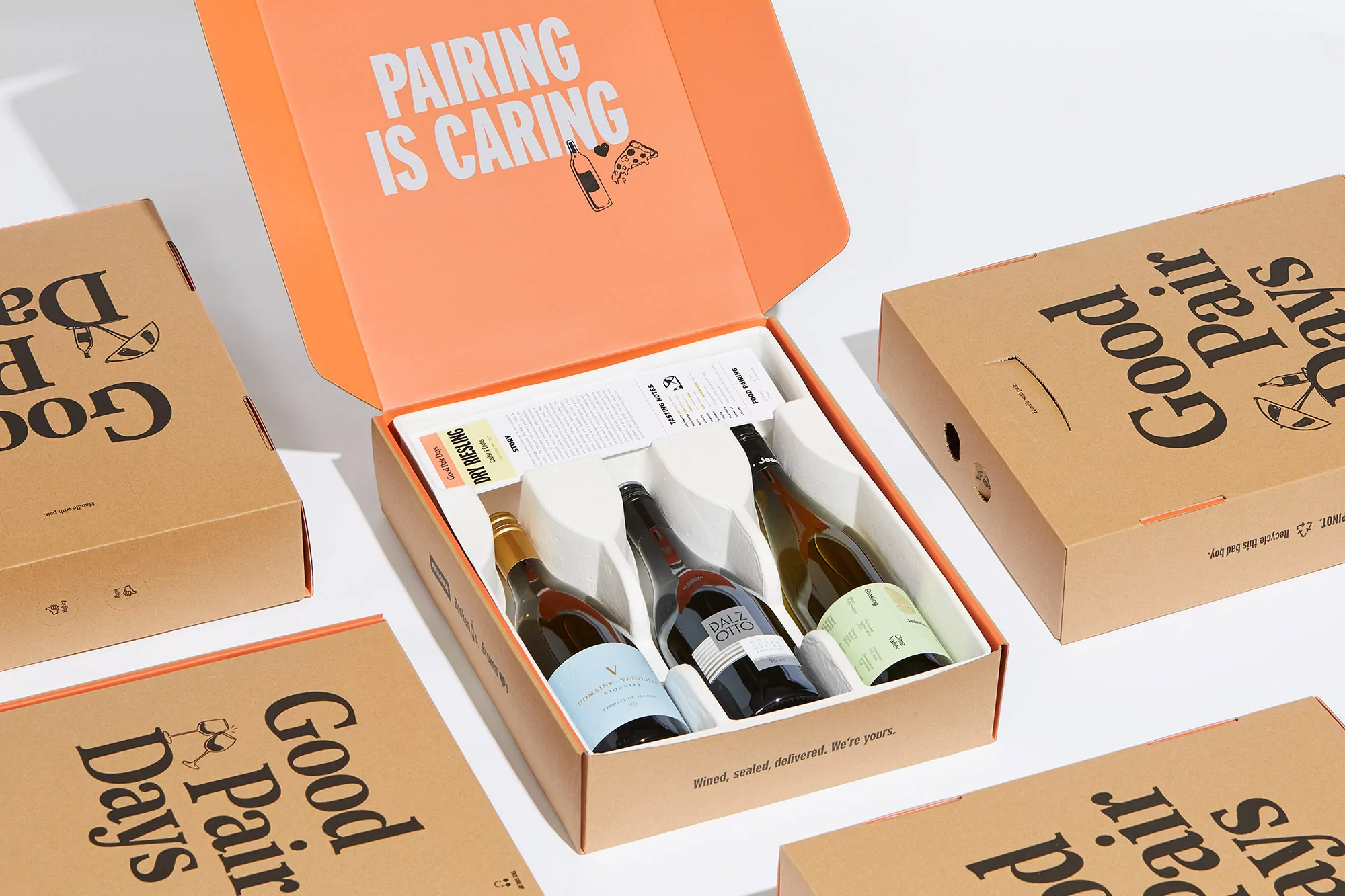 Three bottles of wine presented in a gift box, part of a 'Good Pair Days' subscription, accompanied by sealed boxes, on a white surface.