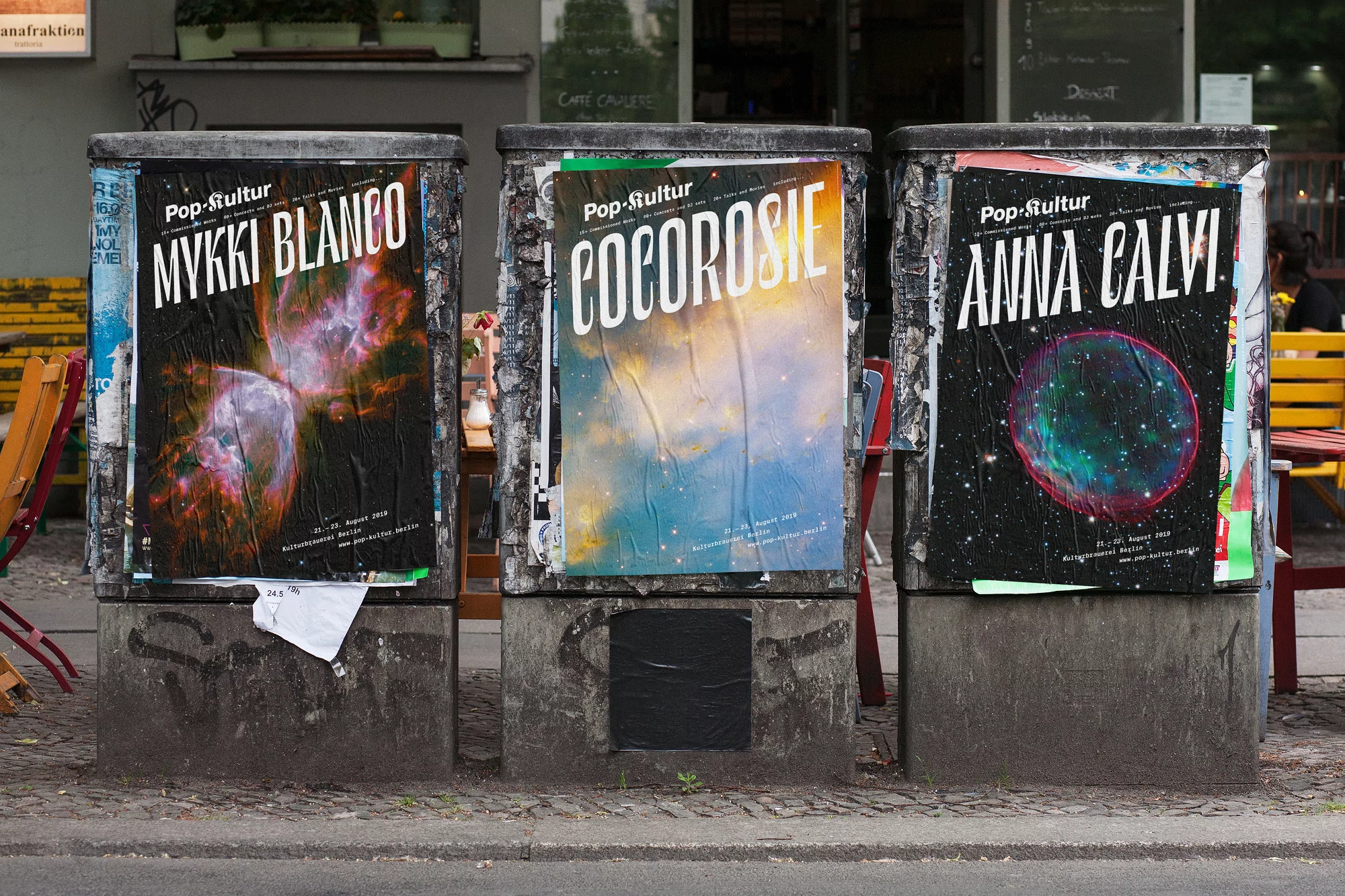 Three outdoor advertisement pillars display concert posters for Mykki Blanco, Cocorosie, and Anna Calvi. Street-level view on a city sidewalk.