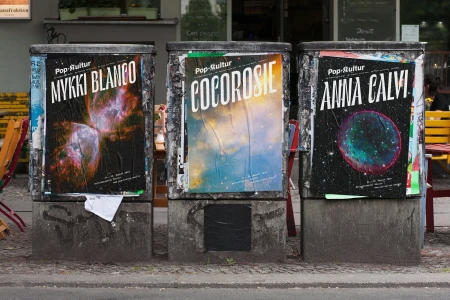 Three posters for Pop-Kultur featuring Mykki Blanco, Cocorosie, and Anna Calvi pasted on concrete utility bins outdoors.