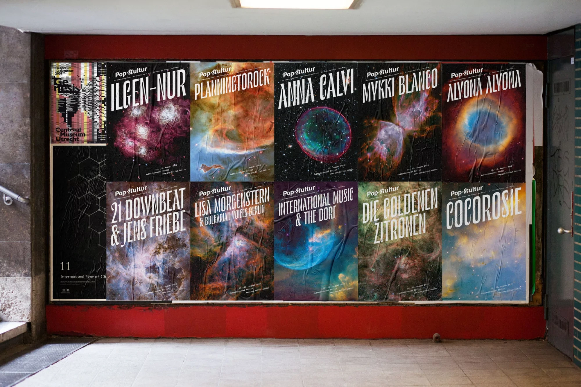 A collage of music festival posters featuring nebula imagery affixed to a red wall in an urban underpass.
