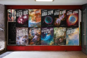 A collage of music festival posters featuring nebula imagery affixed to a red wall in an urban underpass.