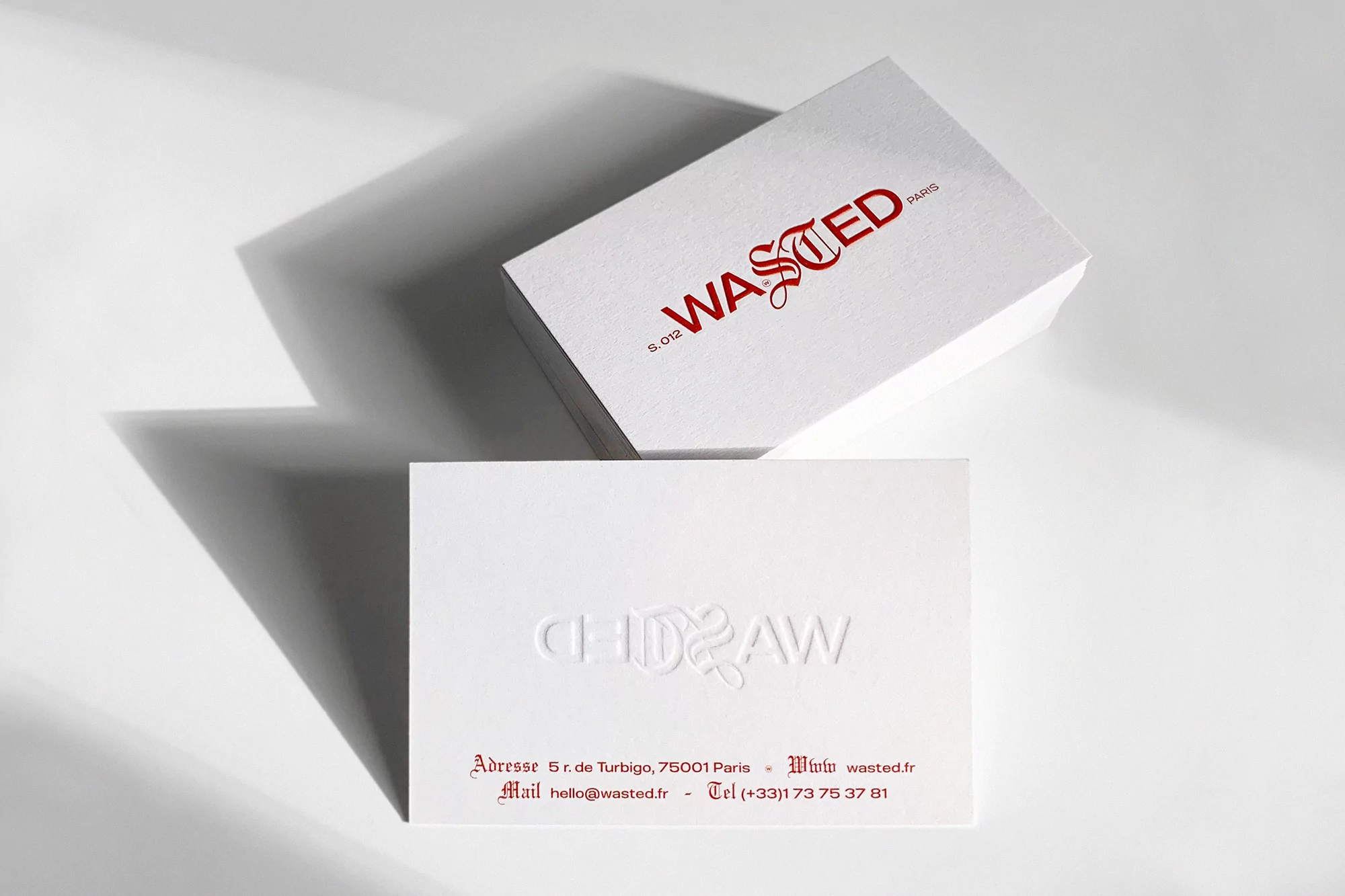 Stack of business cards with 'WASTED' logo in red, embossed text, minimalist design on white surface, studio lighting, brand identity focus.
