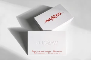 Two white business cards with red typography and embossed logo displayed on a flat surface with strong shadows.