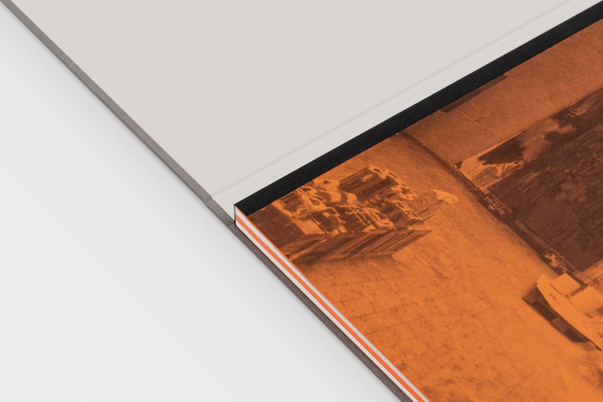 Open book displays an orange-toned image of a building and water, with a light gray cover and black spine, on a white surface.