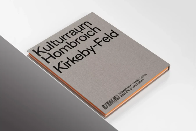 Book titled 'Kulturraum Hombroich Kirkeby-Feld' with a grey cover, black sans-serif text, and orange edges, casting a soft shadow.