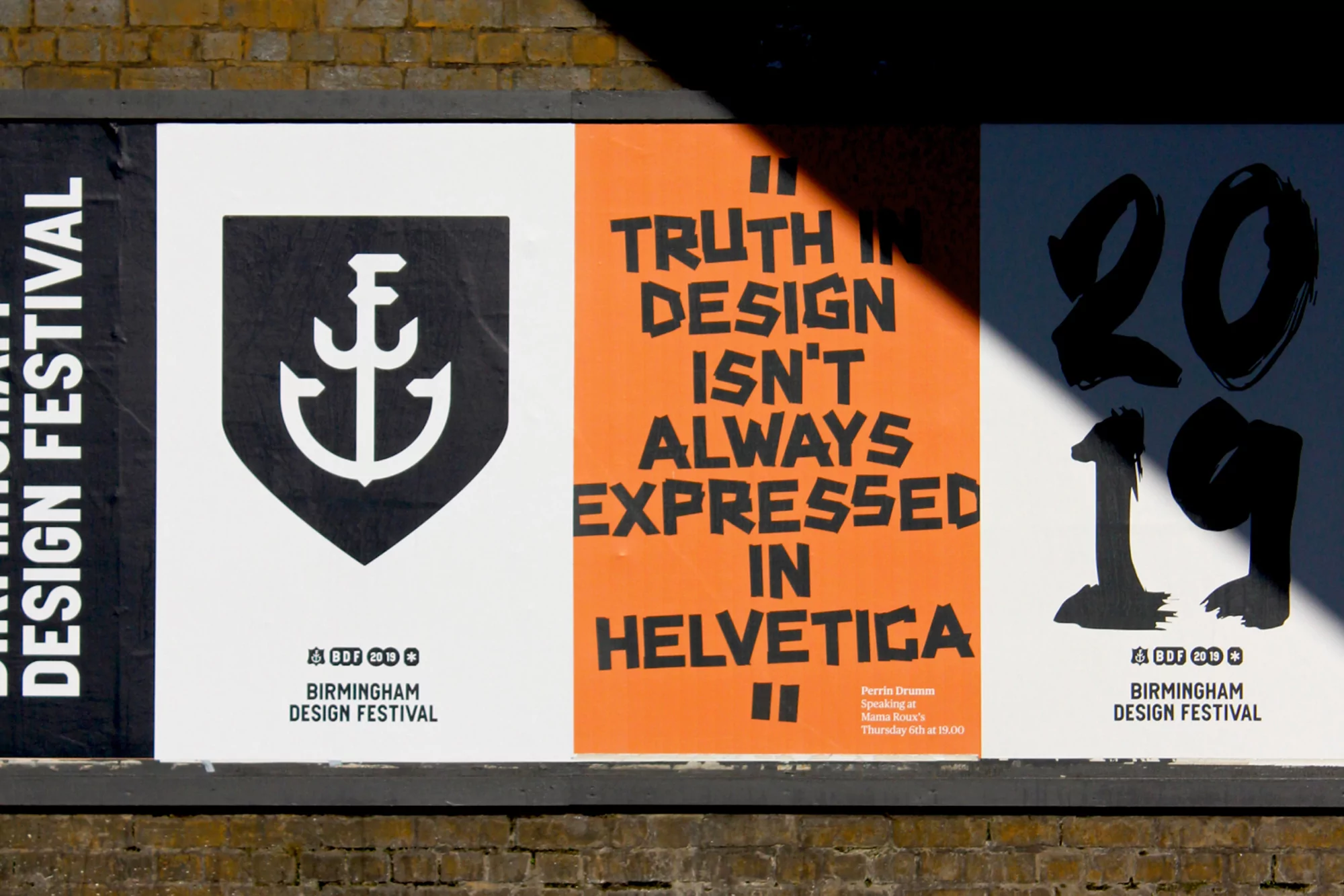 Birmingham Design Festival posters on an outdoor brick wall: anchor logo, typographic poster, 2019 year poster, and natural daylight.