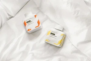 Two white medicine bottles with orange and yellow graphic labels resting on folded white fabric