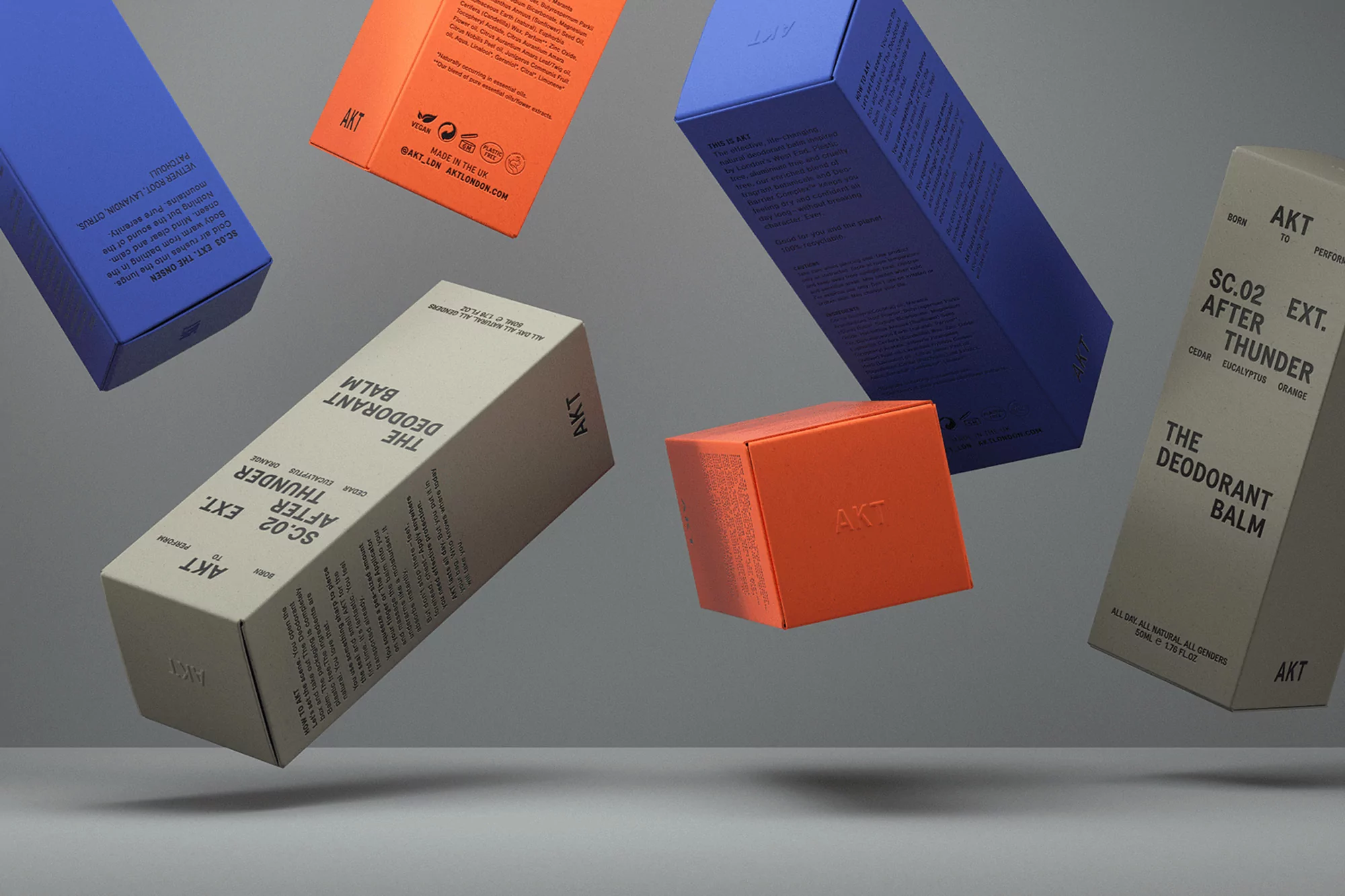 Close-up studio shot of colorful deodorant balms in orange, blue, and beige boxes, artfully arranged on a gray background.