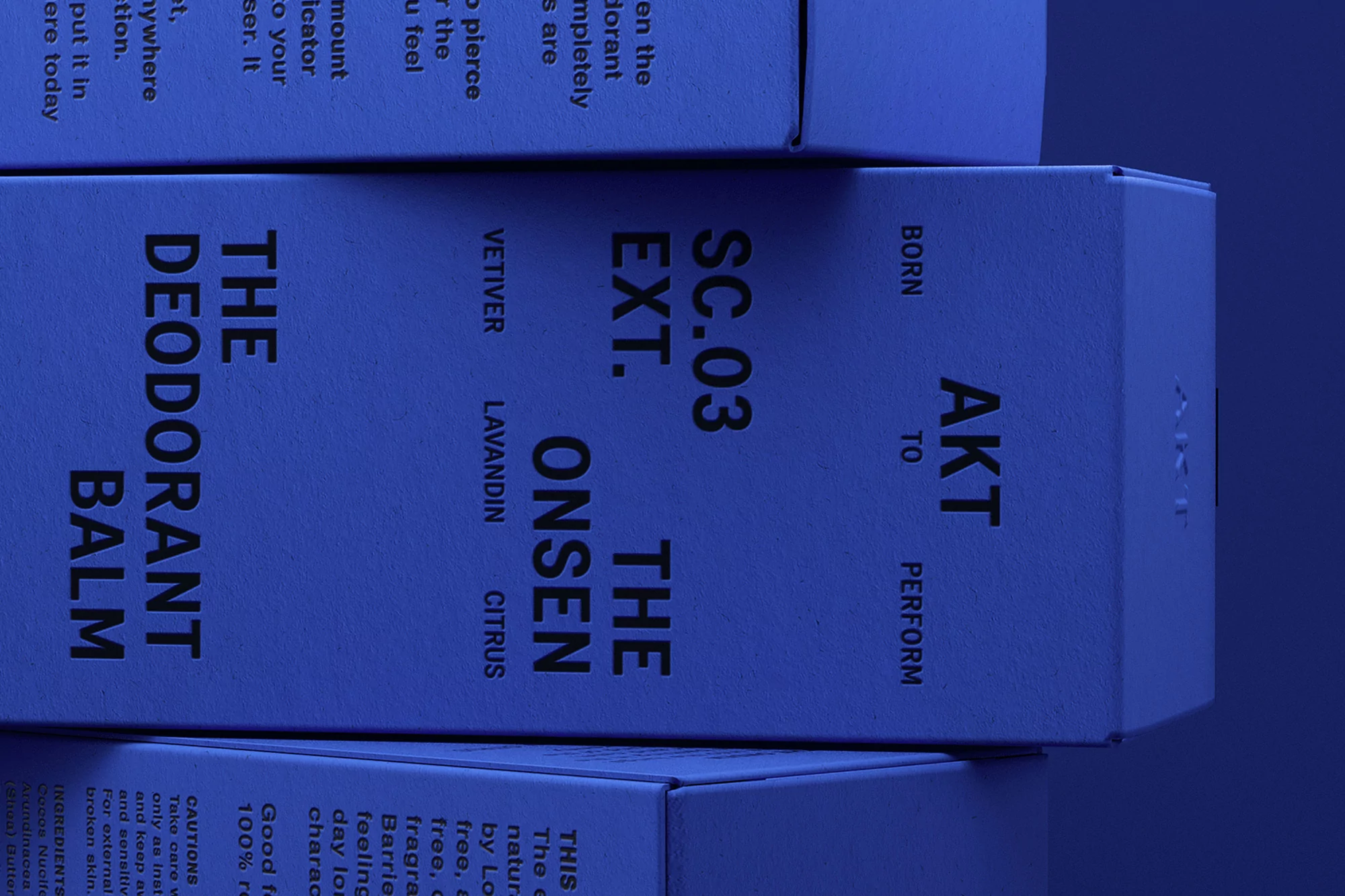 Stacked boxes of AKT The Deodorant Balm beauty product, featuring label details like 'SC.03 EXT. THE ONSEN' and scent names.