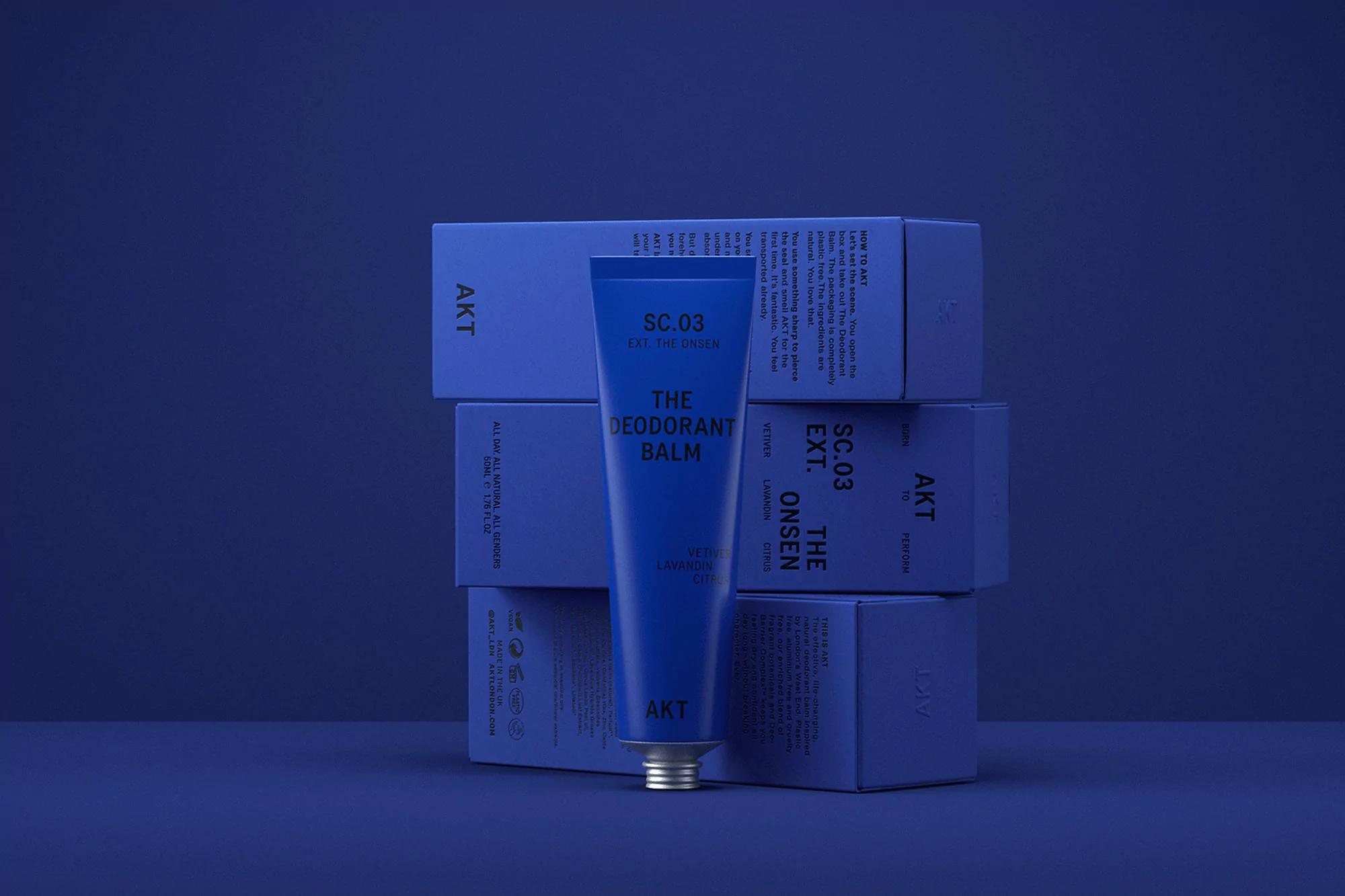 Blue tube of deodorant balm on a matching blue background with deodorant boxes. The focus is on the product and its minimalist packaging.