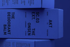 Blue product packaging boxes for AKT deodorant stacked against a monochrome blue background