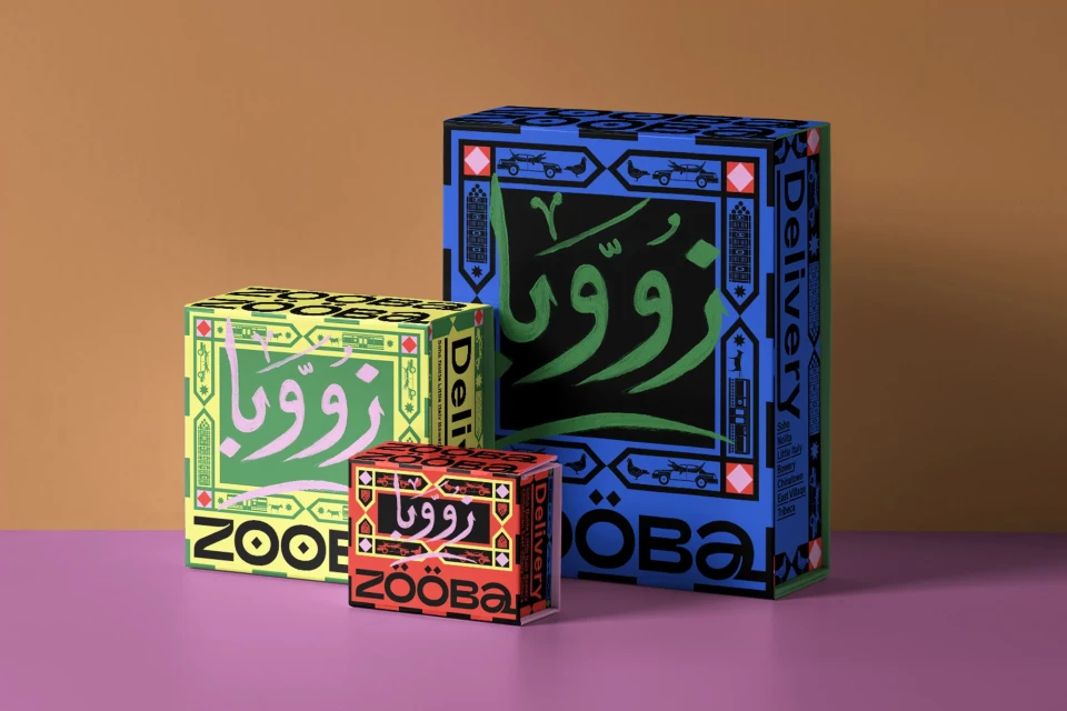 Three product boxes of varying sizes, designed with colorful patterns and Arabic script, sit on a purple surface against a tan backdrop.