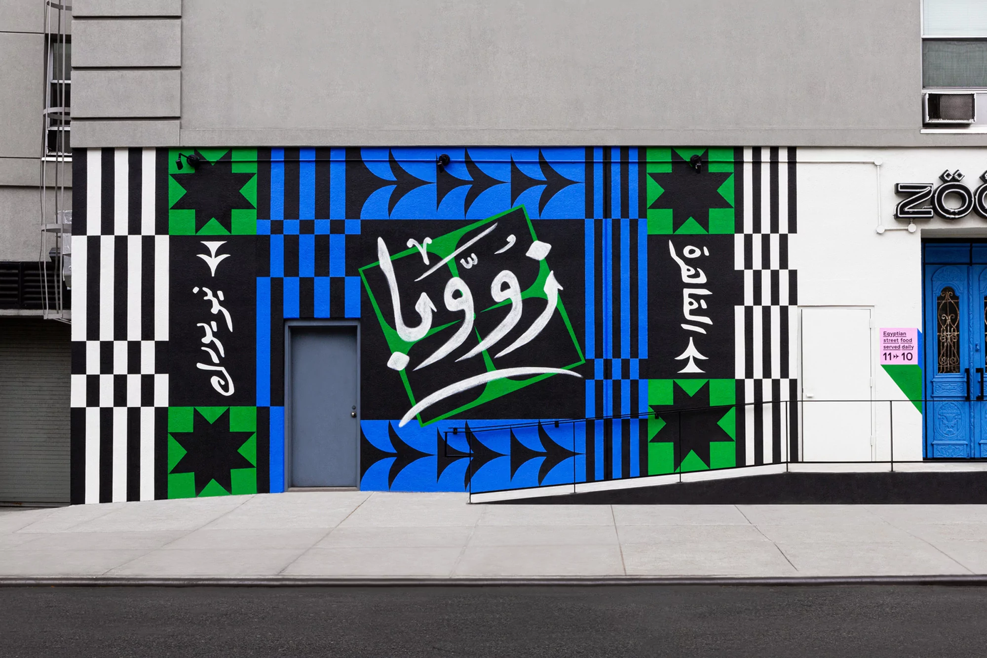 Exterior mural with geometric patterns in black, green, and blue. Arabic script is incorporated, adding a cultural element to the artwork.