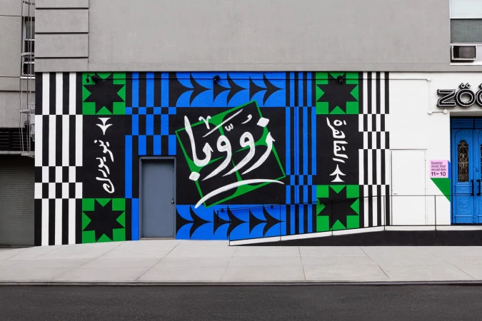 Exterior mural with geometric patterns in black, green, and blue. Arabic script is incorporated, adding a cultural element to the artwork.