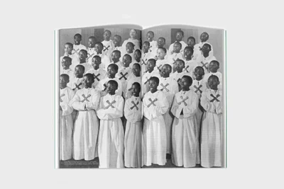 Open book page showing a black and white photograph of a large choir of children wearing white robes with crosses.