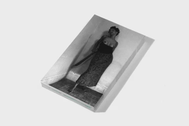 A stacked pile of printed publications angled on a plain surface, displaying a black and white portrait of a woman.