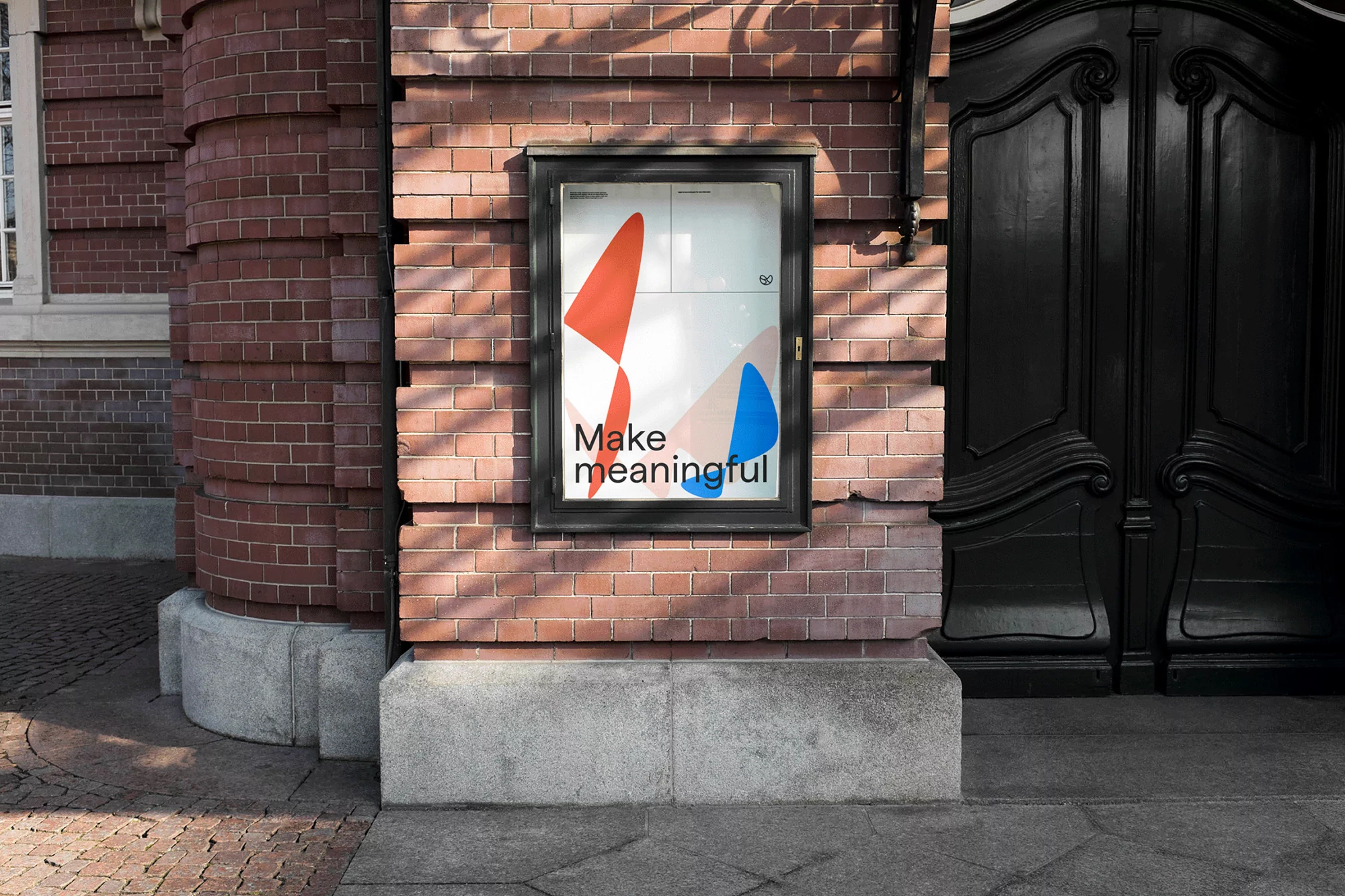 Outdoor poster on a brick wall featuring red and blue geometric shapes, set against a solid black door, showcasing urban design.