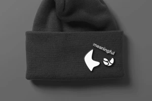 Dark grey knit beanie with white embroidered brand logo and the word meaningful on the folded brim