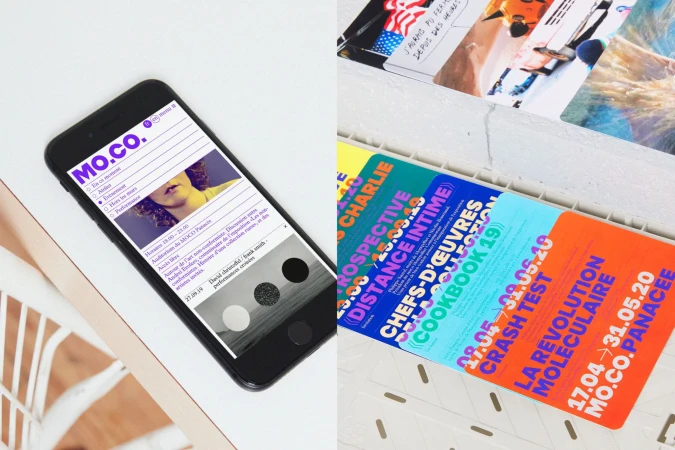 Mobile phone displays the MO.CO website with art events alongside printed promotional cards on a white surface. 