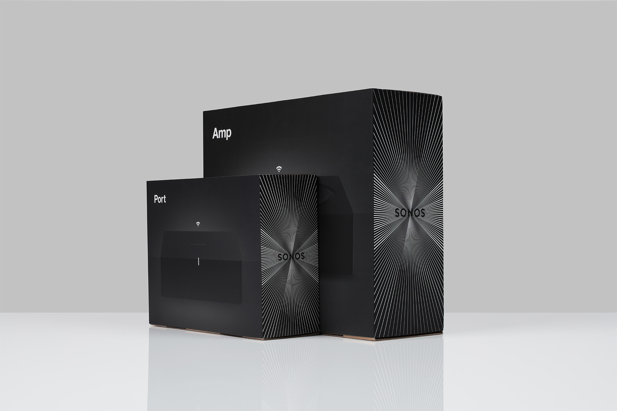 Two black Sonos boxes, one labeled 'Port' and the other 'Amp,' stand on a reflective white surface against a gray backdrop.