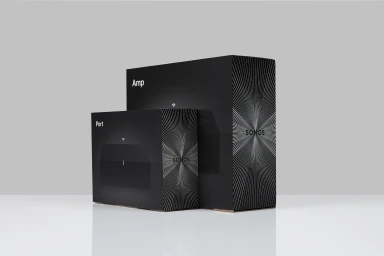 Sonos audio product packaging boxes in black with geometric wave patterns displayed on a white reflective surface.