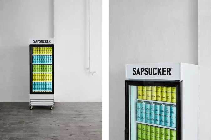 Two refrigerators stocked with blue, green, and yellow canned drinks against a white wall in an indoor setting, showcasing a clean aesthetic.