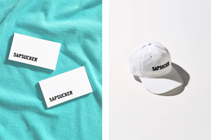 Minimalist product shot featuring a white baseball cap and two business cards on a split white and teal background, clean aesthetic.